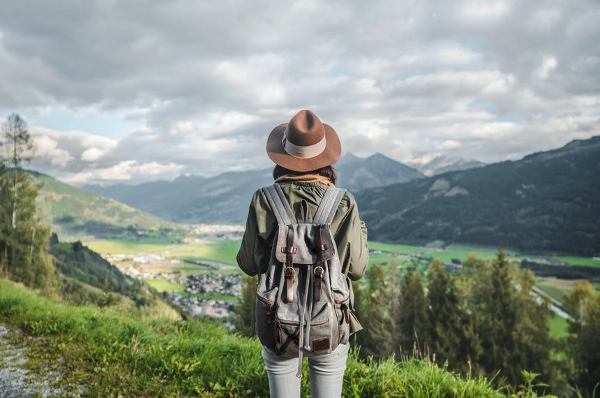 Viajero con mochila mirando un paisaje de montaña andino mientras consulta el mapa en su teléfono