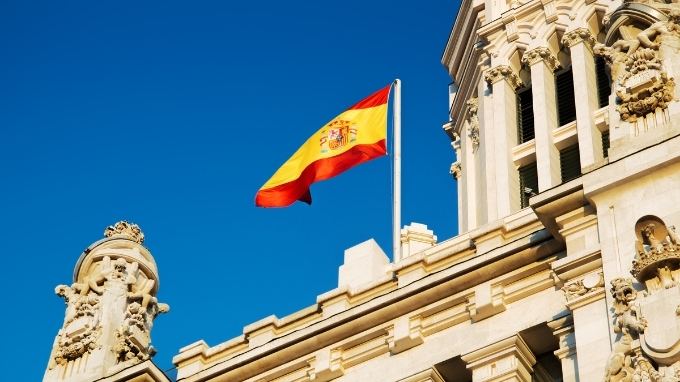Edificio histórico con la bandera de España ondeando bajo un cielo azul