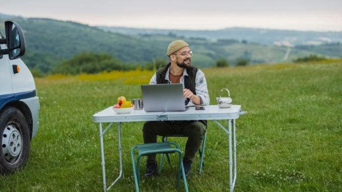 Nómada digital trabajando con su laptop en una mesa plegable junto a una furgoneta, en el campo