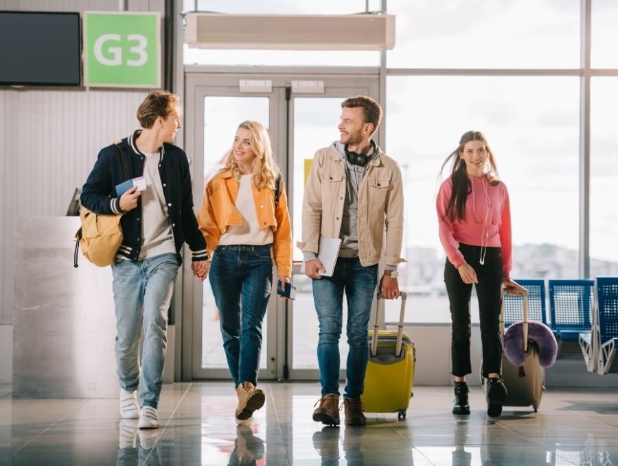 Cuatro amigos caminando juntos por un aeropuerto con sus maletas
