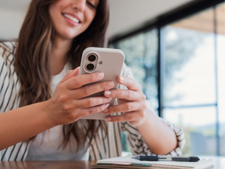 Mujer sonriendo mientras escribe en su teléfono