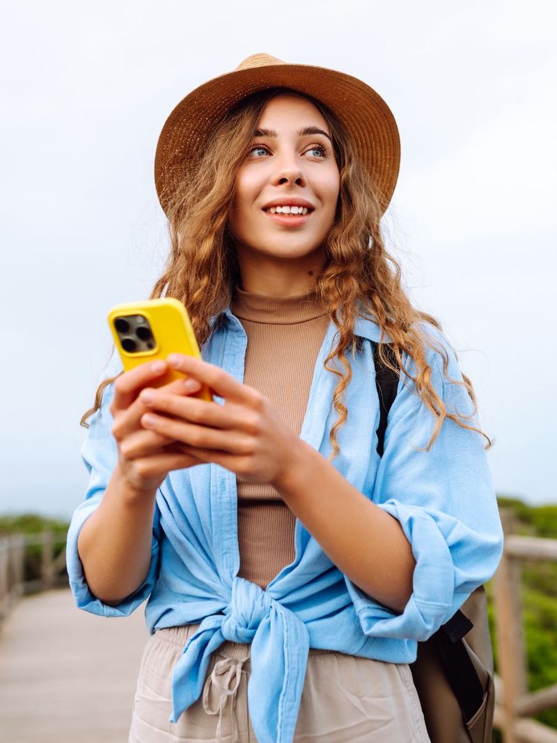 Viajera con sombrero y camisa azul sonriendo con su teléfono en la mano